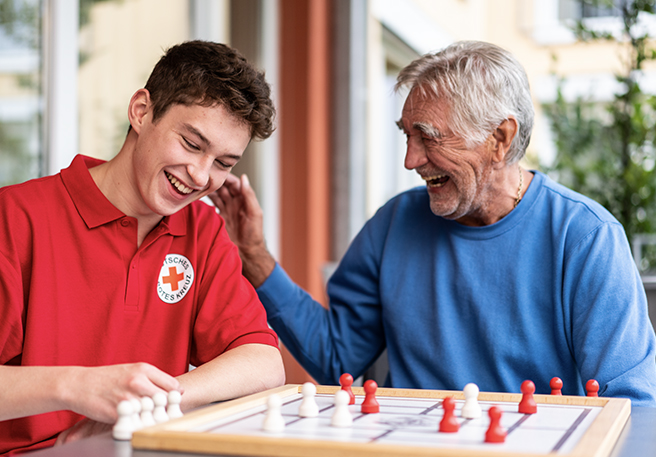 DRK-Mitarbeiter und Senior spielen gemeinsam ein Brettspiel