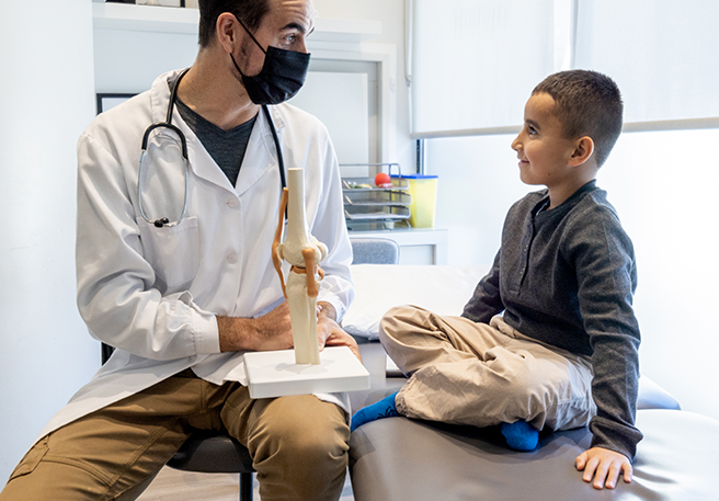 Arzt zeigt einem Jungen eine Knie-Nachbildung