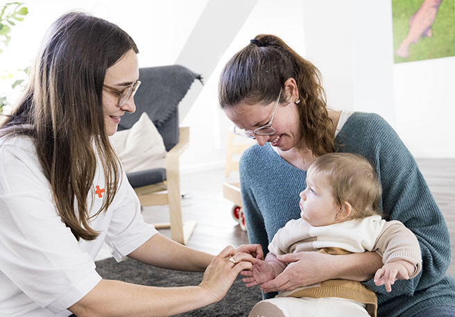 Hebamme untersucht Säugling auf dem Schoß seiner Mutter